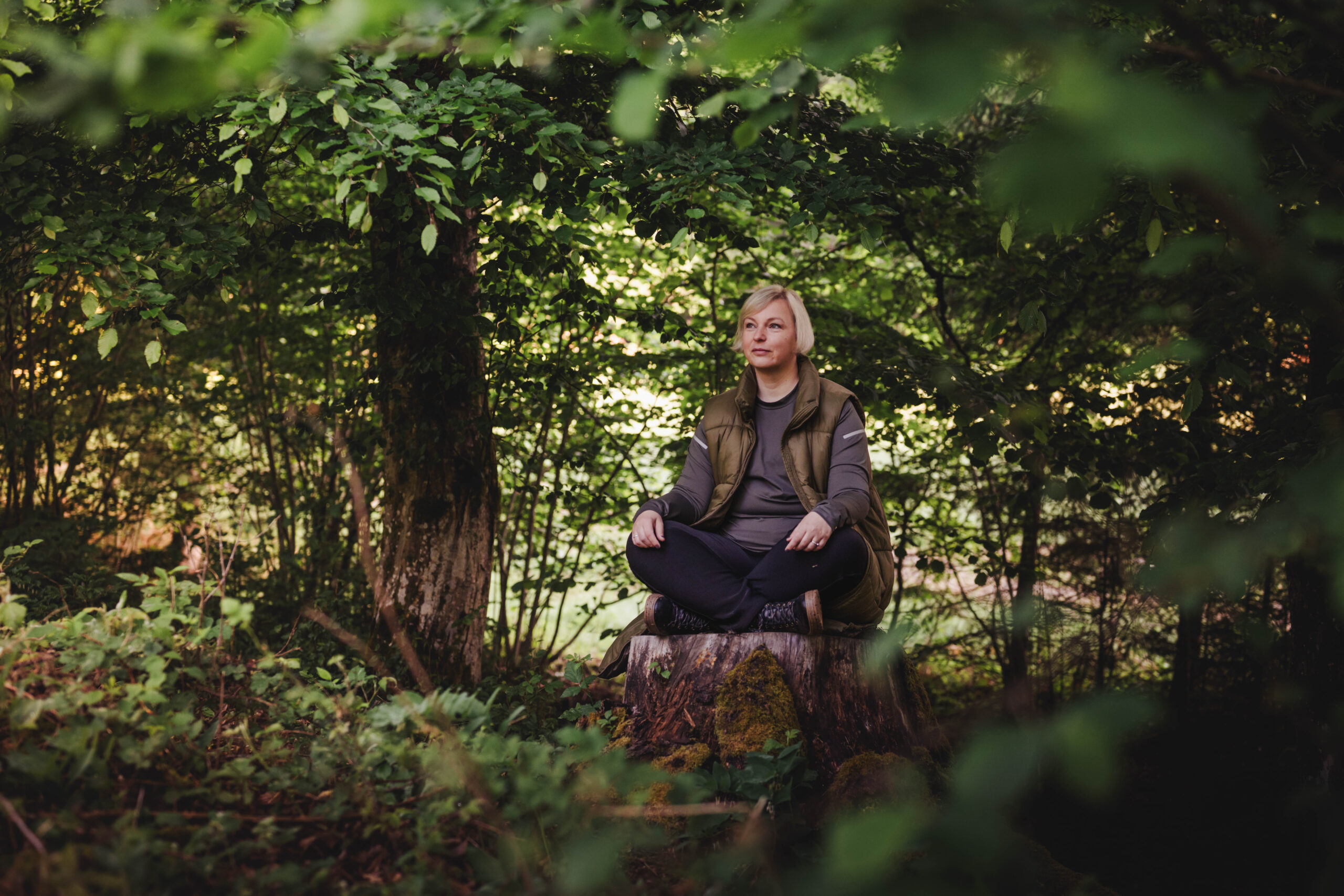 A woman sitting quietly on a tree stump, listening to the forest around her
